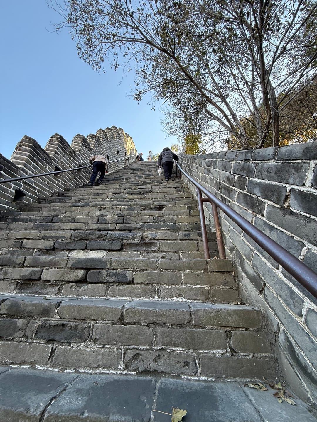 Una ripida scalinata di pietra sulla Grande Muraglia a Badaling, con un corrimano e alcuni visitatori che salgono