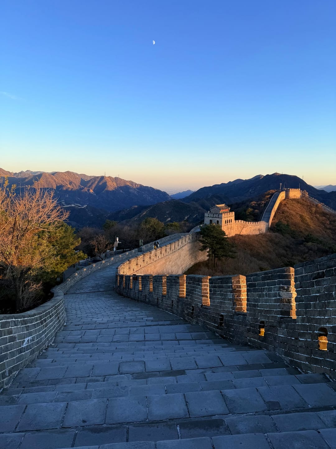 Die Große Mauer bei Badaling im Licht des späten Nachmittags, ein gepflasterter Wehrgang führt zu einem Wachturm auf dem Grat