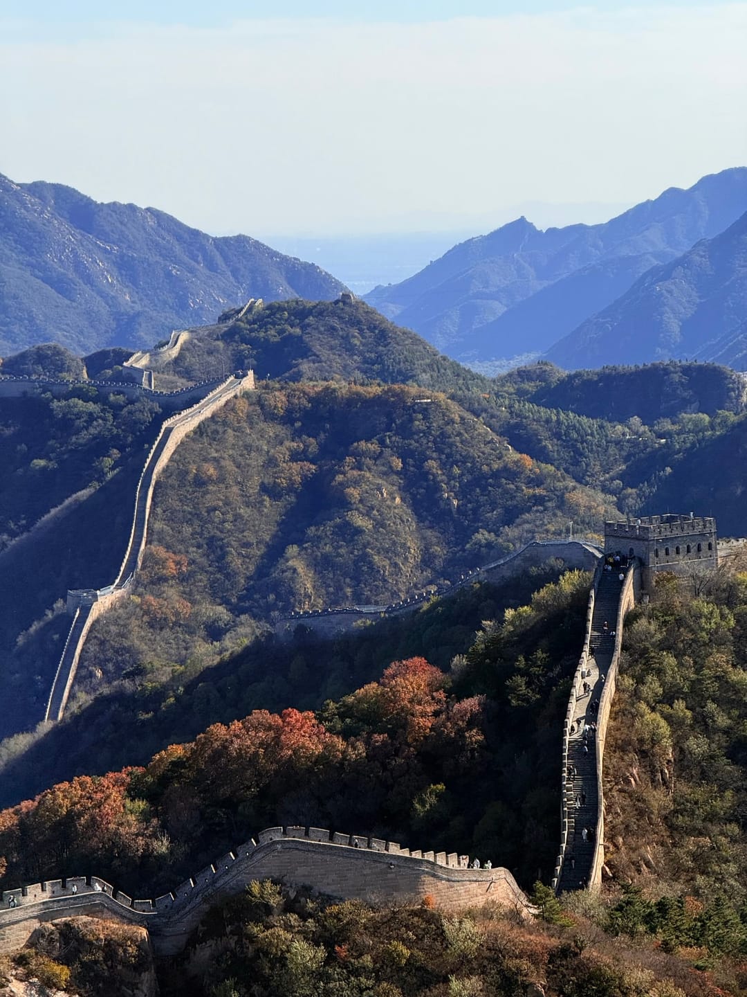The Great Wall at Badaling winding along a mountain ridge in autumn colours, with watchtowers and further ridges behind