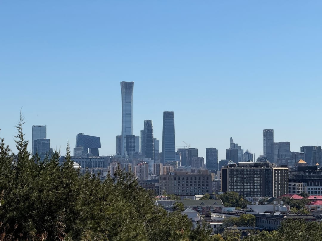 The towers of Beijing’s business district under a blue sky, seen over trees from the summit of Jingshan Park