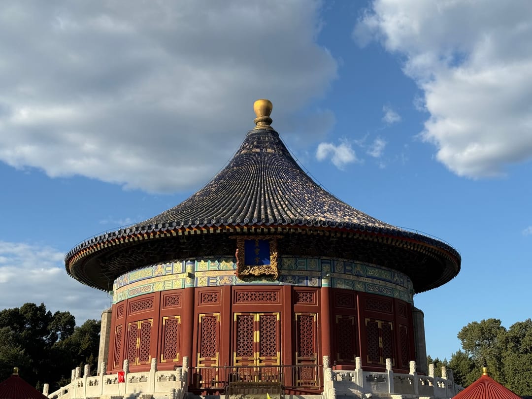 The round Imperial Vault of Heaven with its blue conical roof and gold finial, under a blue sky with white clouds