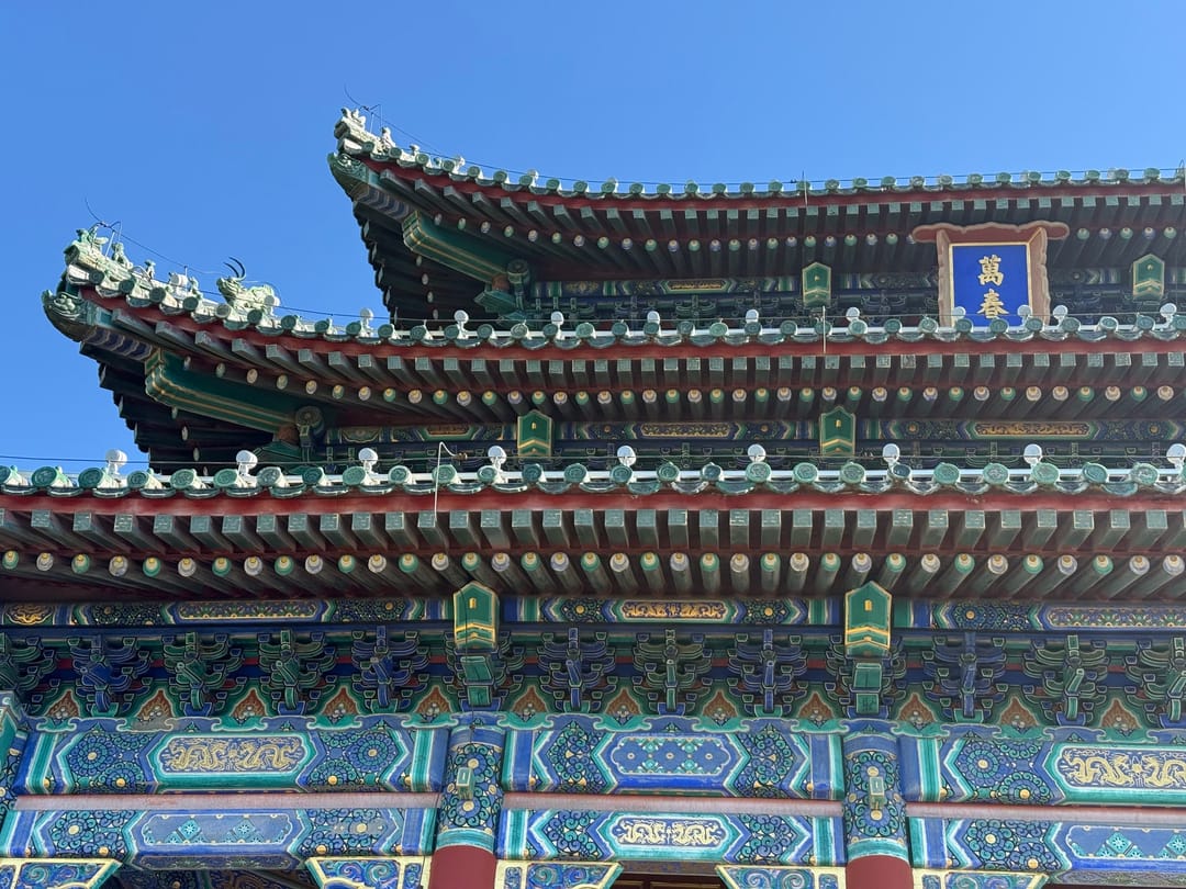 Tejados de varios niveles de un pabellón del parque Jingshan, con vigas pintadas de verde y azul y una placa azul en lo alto