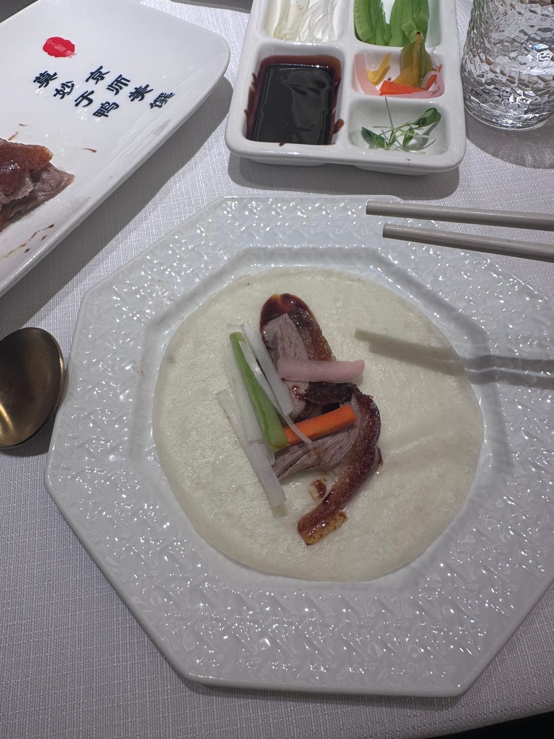 Ein dünner Pfannkuchen auf einem Teller, belegt mit Pekingente, Gurke und Frühlingszwiebel