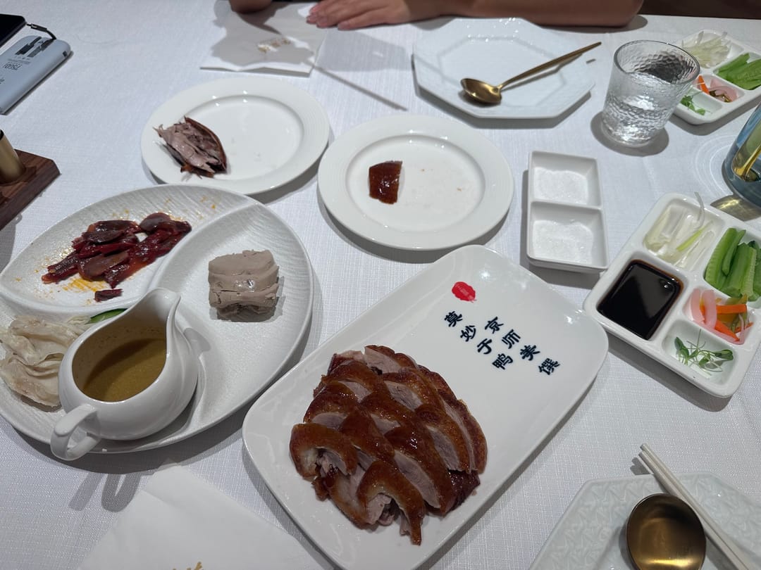 Sliced Peking duck on a white platter, with small dishes of sweet bean sauce, scallion, cucumber and pickles on a restaurant table