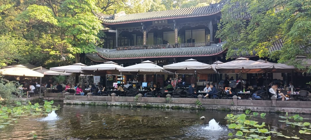 Mesas bajo sombrillas blancas en la terraza junto al lago de una casa de té de madera de dos plantas, en el Parque del Pueblo