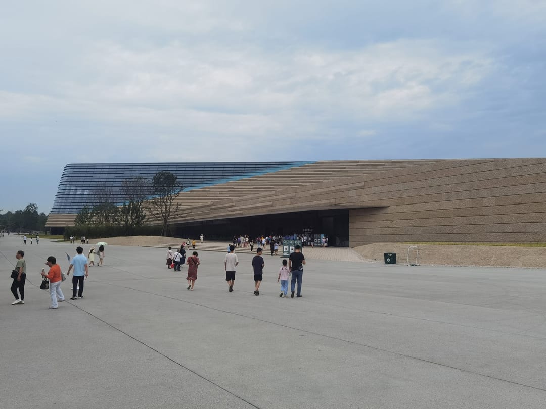 Visitantes cruzan una amplia explanada hacia el tejado largo, bajo e inclinado de la nueva sala del Museo de Sanxingdui