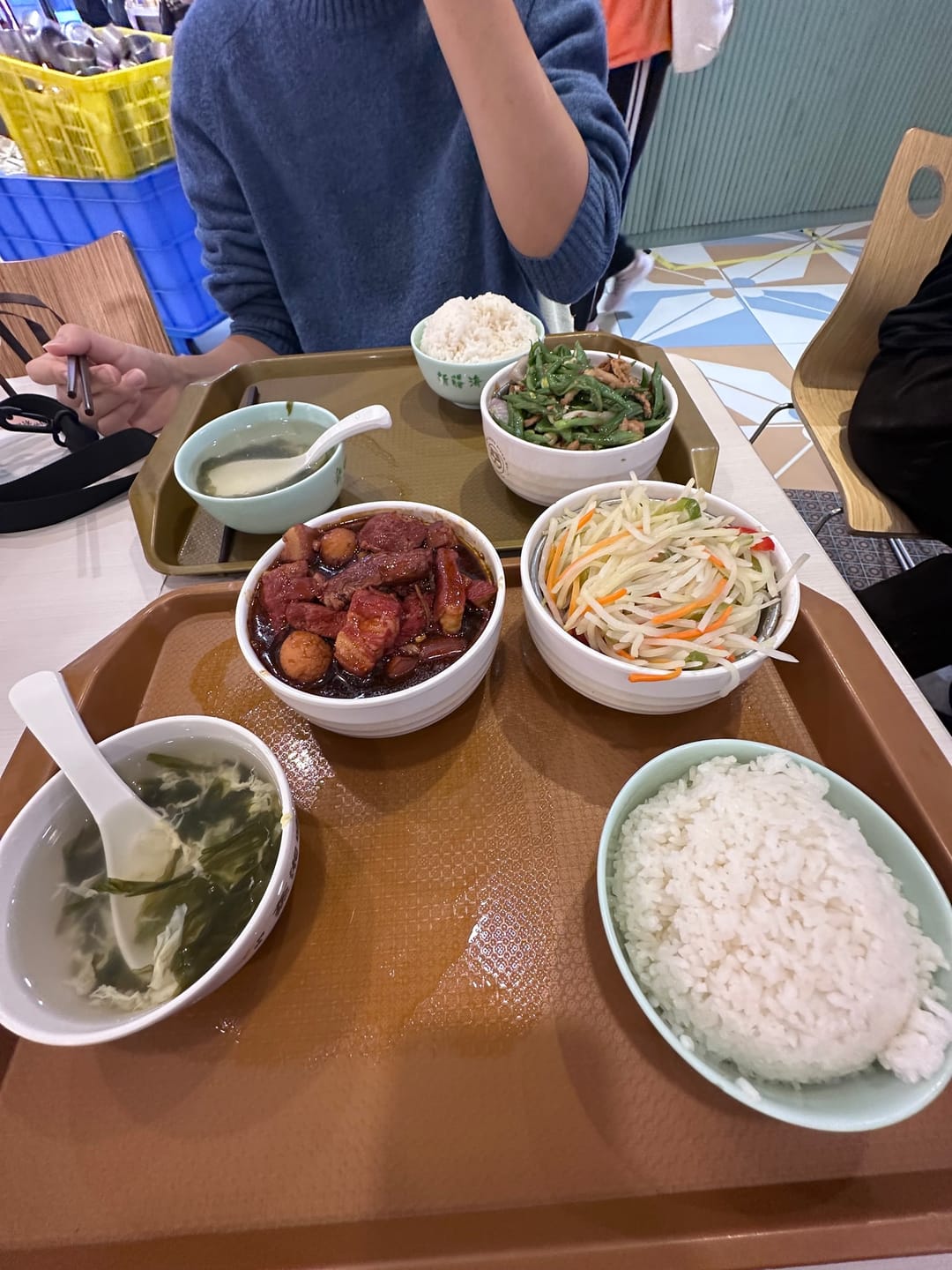 A canteen tray with rice, braised pork, a shredded vegetable salad, stir-fried green beans and a bowl of seaweed soup