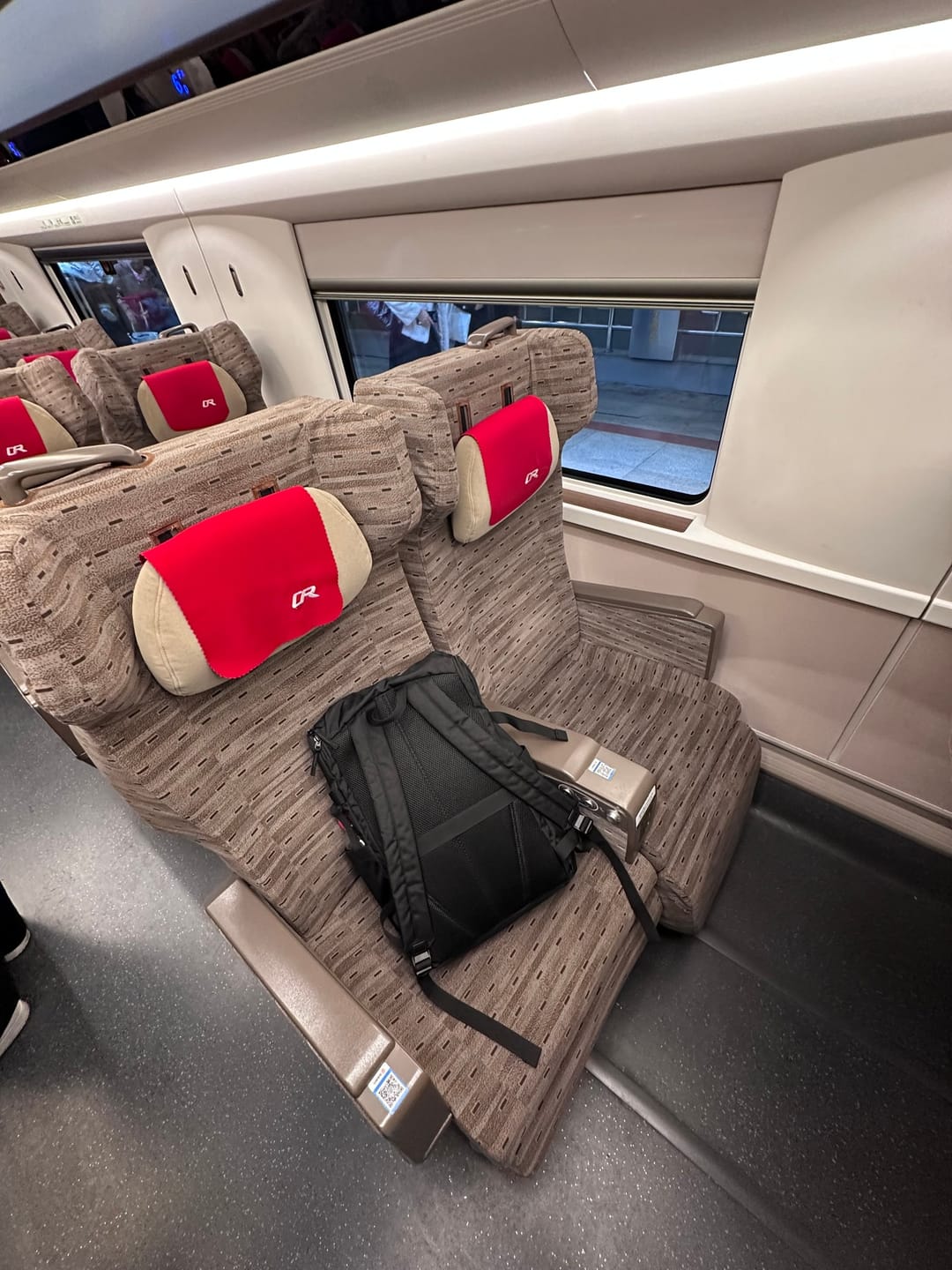 Second-class seats with red headrest covers on a Chinese high-speed train, a backpack on one seat by the window