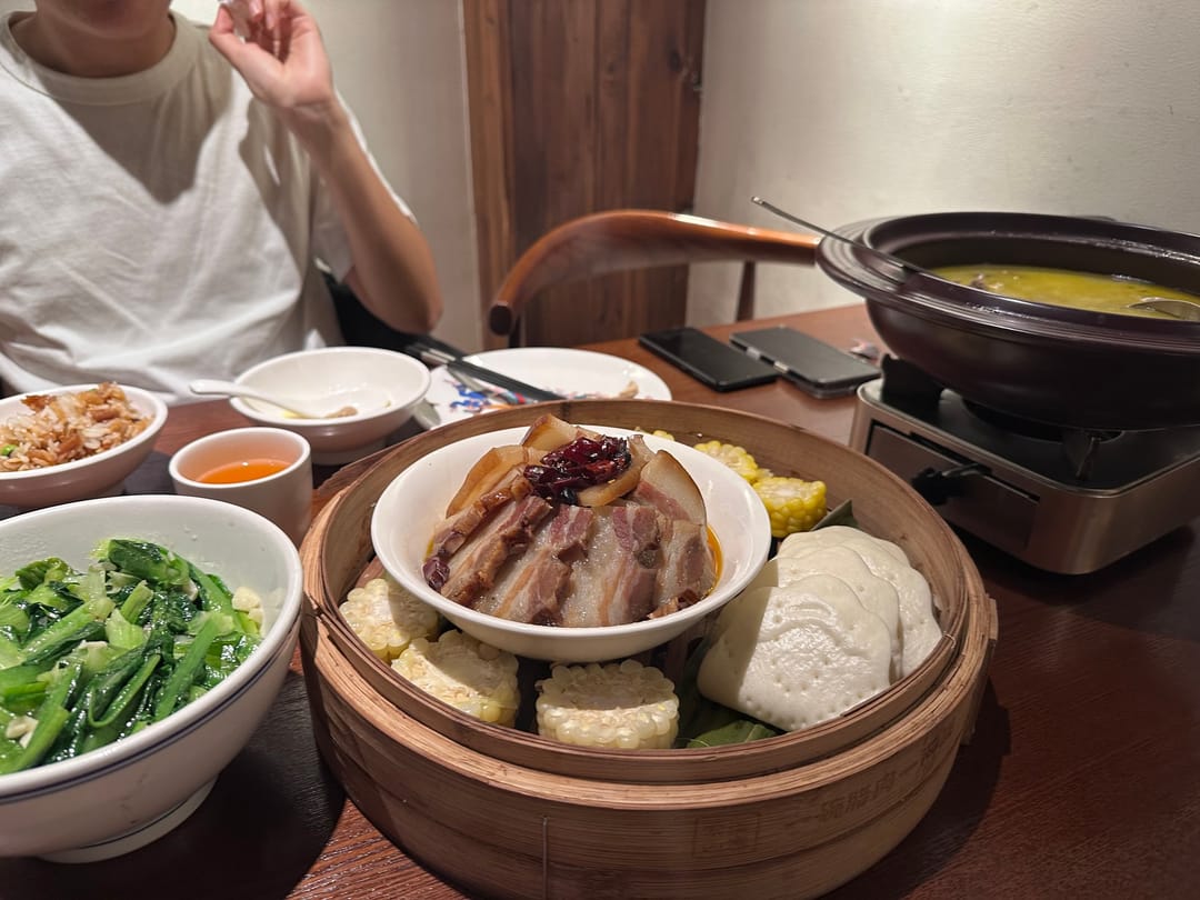 Ein Restauranttisch in Wulingyuan mit geräuchertem Schweinefleisch auf einem Dämpfkorb, gebratenem Grüngemüse und einem Topf Suppe