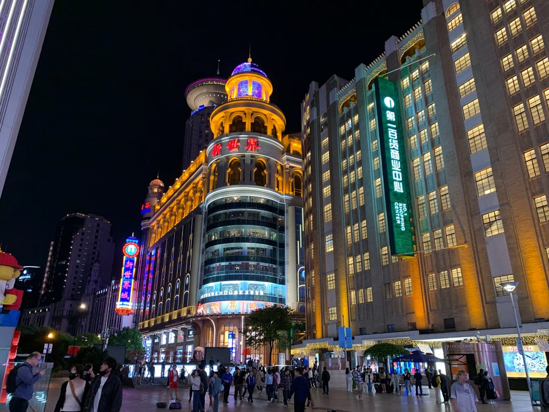 East Nanjing Road in Shanghai at night, a domed department store lit in gold and neon signs along the street