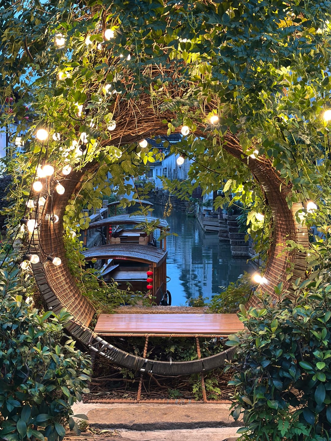 Un arco redondo de mimbre con luces enmarca un canal del casco antiguo de Suzhou, con una barca de madera amarrada abajo