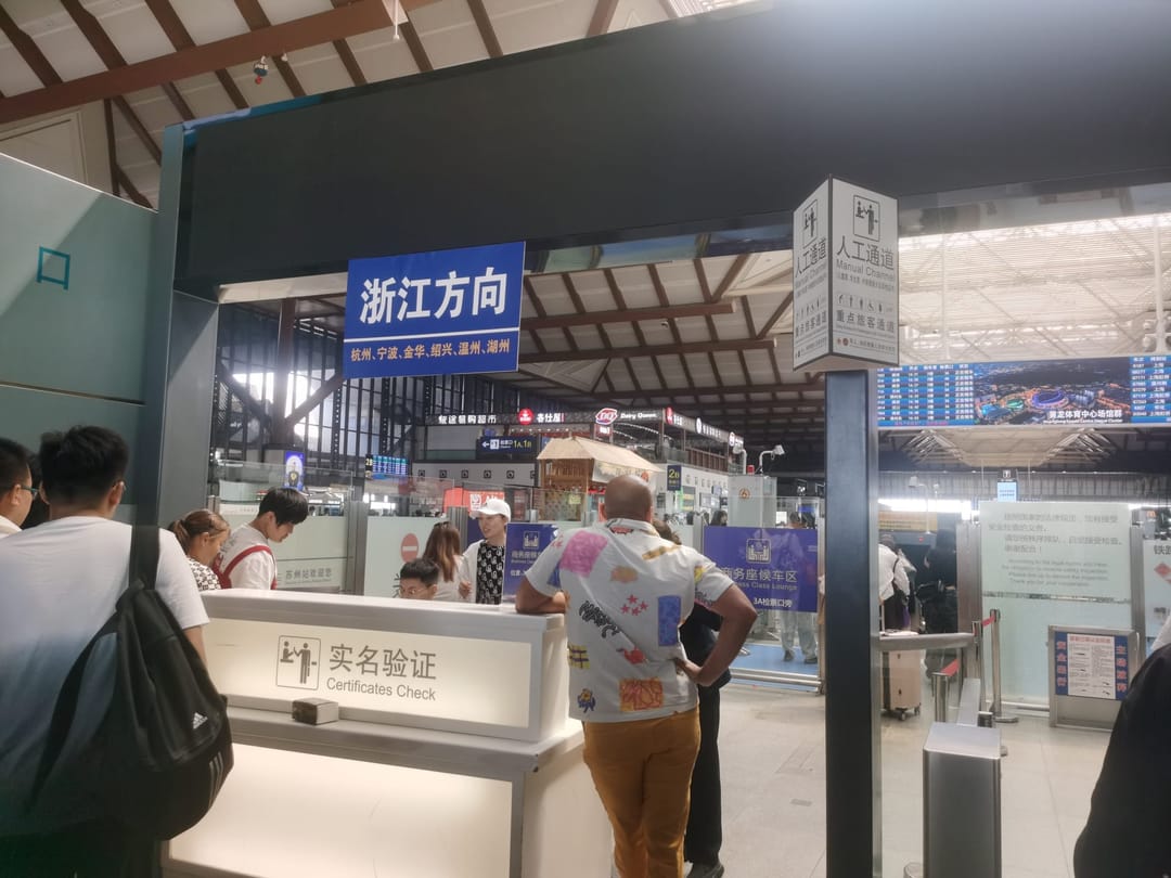 Passengers queuing at a counter marked Certificates Check in Suzhou railway station, next to a sign reading Manual Channel