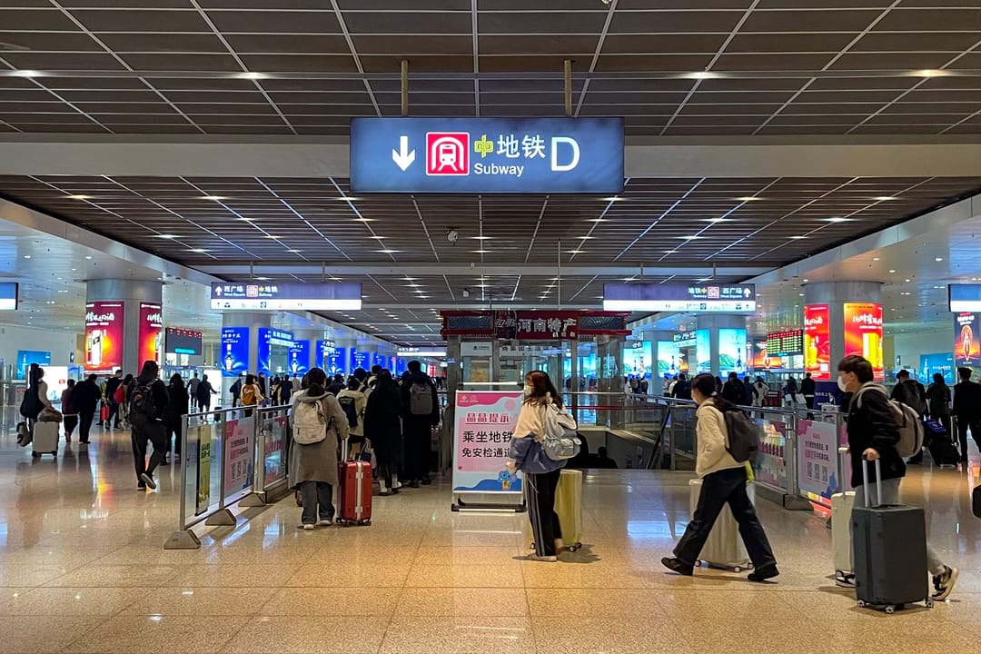 Reisende mit Rollkoffern in der Halle des Bahnhofs Zhengzhou Ost, über ihnen ein Schild zur U-Bahn