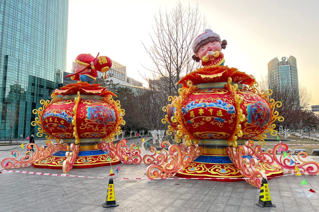 Two giant red lanterns topped with smiling child figures on a plaza between office towers on Beijing’s Financial Street