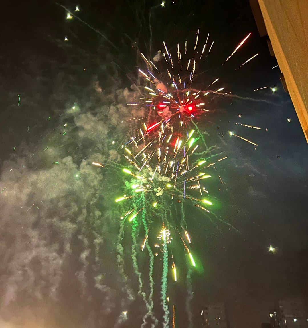 Green, red and gold fireworks bursting in a dark sky over a village on the edge of Fuzhou at midnight