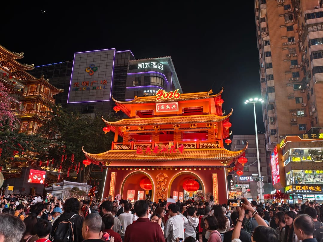 A lit red gateway with a 2026 sign above a dense evening crowd at the Yuexiu flower fair in Guangzhou
