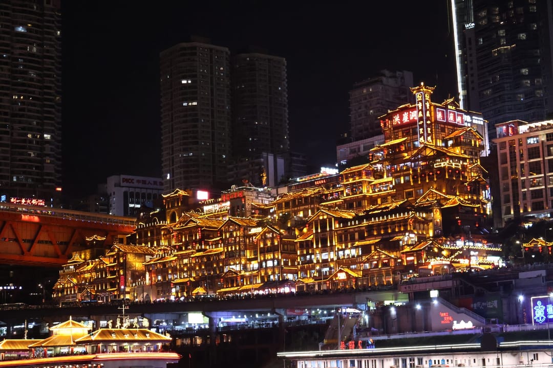 Los pisos de casas sobre pilotes de Hongyadong, iluminados de dorado sobre el Jialing, con barcos amarrados y torres detrás