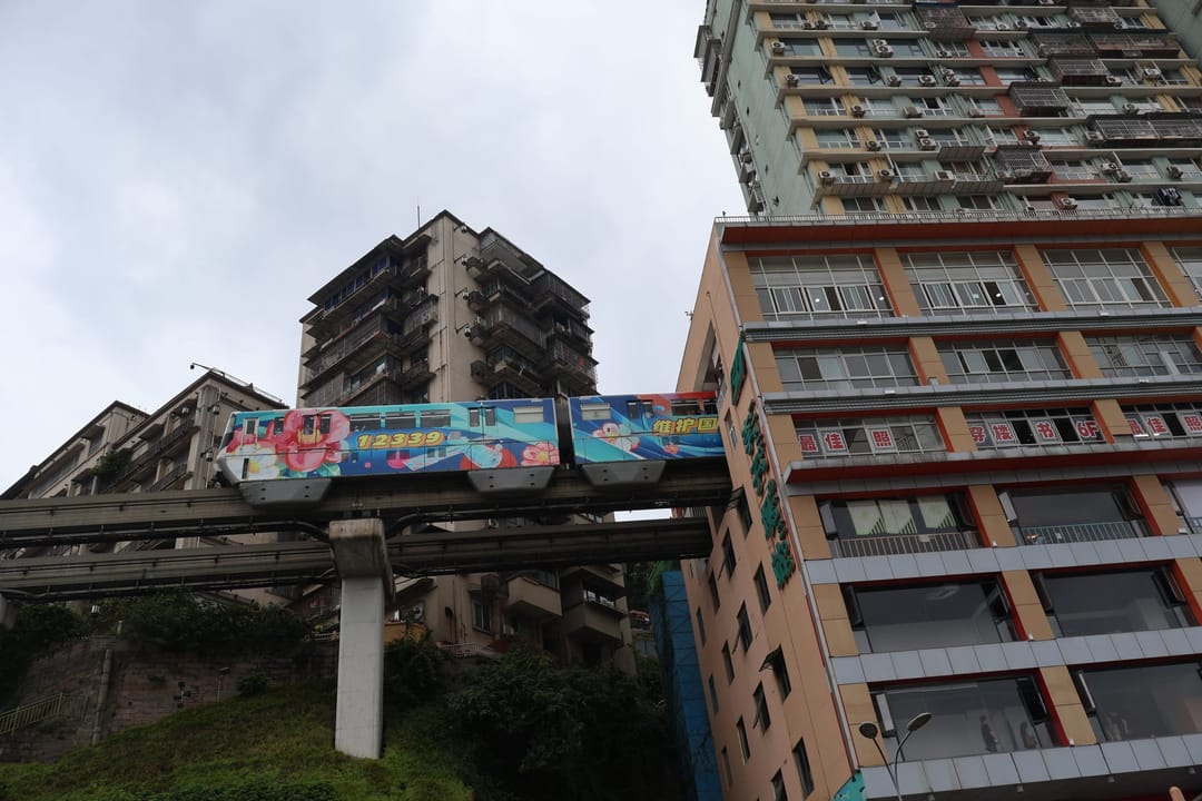 Un tren pintado del monorraíl de la línea 2 avanza por su vía elevada hacia la torre de viviendas que alberga la estación