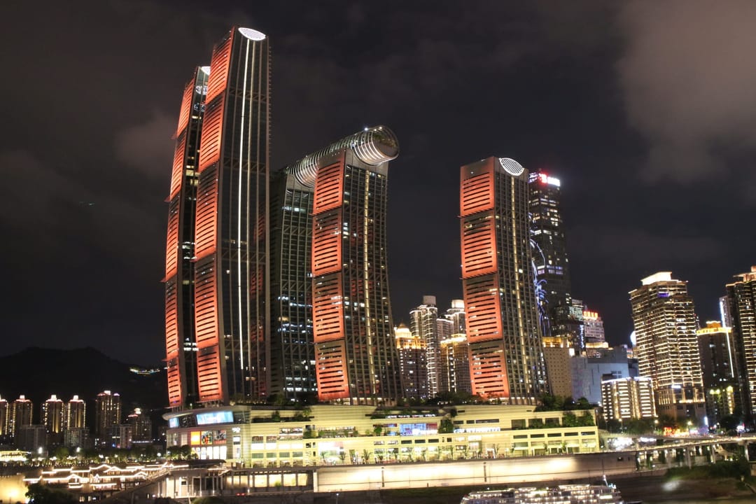 Las torres curvas de Raffles City iluminadas de rojo de noche en la punta de la península, unidas en lo alto por un puente