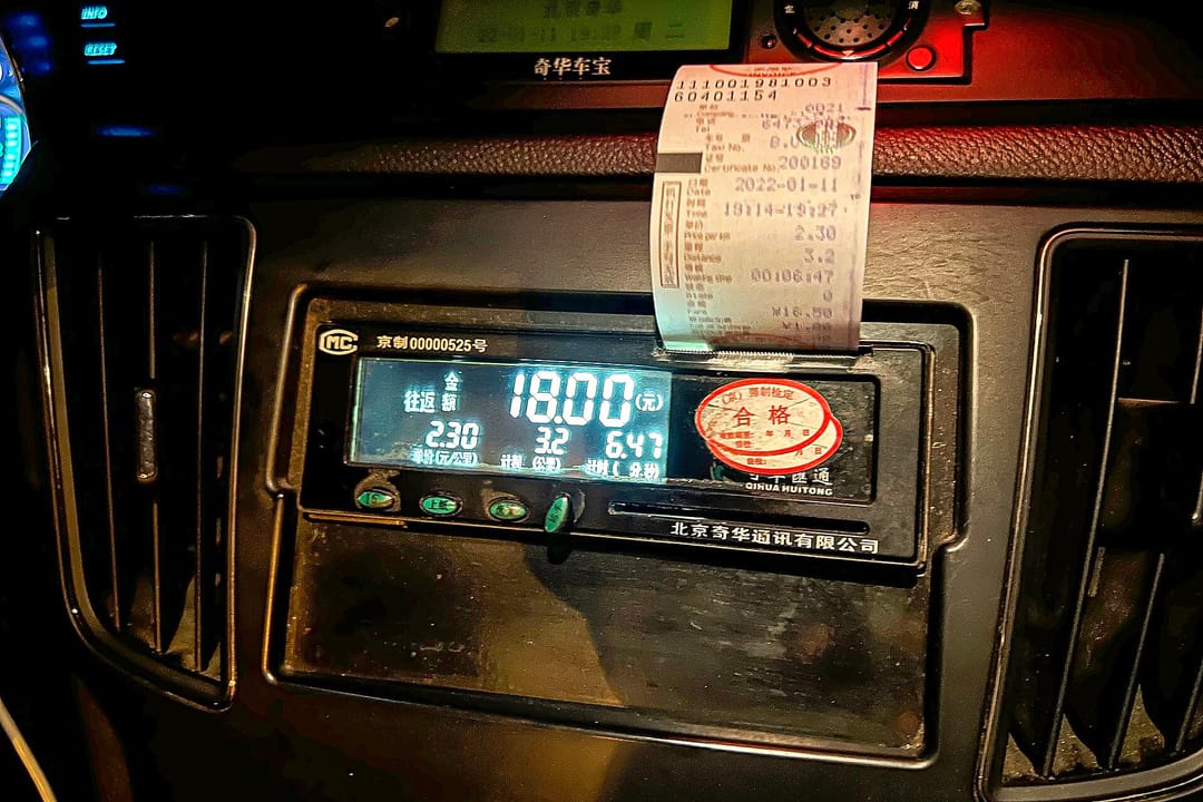 Un taxímetro de Pekín que marca 18 yuanes por 3,2 km a 2,30 yuanes el kilómetro, con un recibo de papel saliendo encima