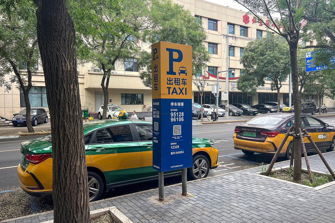 Cartel de una parada de taxis de Pekín con los números de reserva 95128 y 96106, y taxis verdes y amarillos detrás