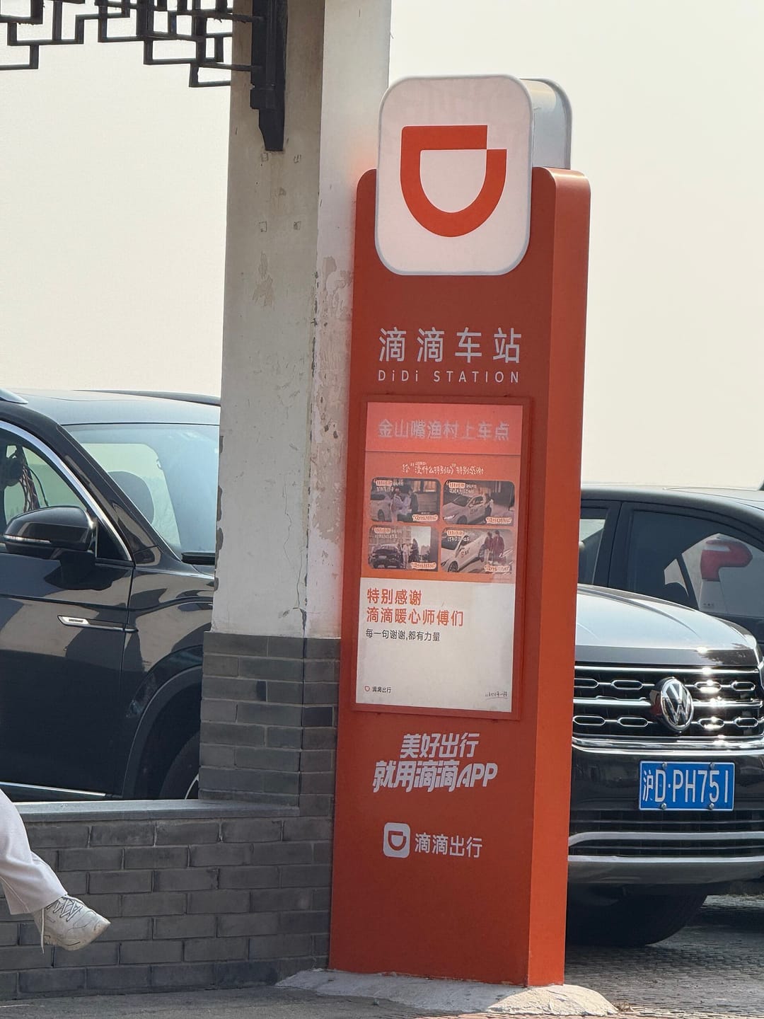 Un cartel naranja de DiDi Station con el logotipo de DiDi que señala un punto de recogida junto a coches aparcados