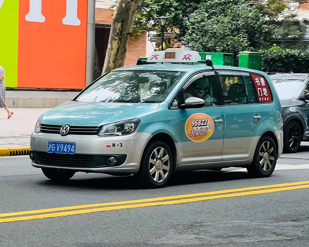 Un taxi turquesa de Dazhong, un Volkswagen Touran con luminoso en el techo, circulando por una calle de Shanghái