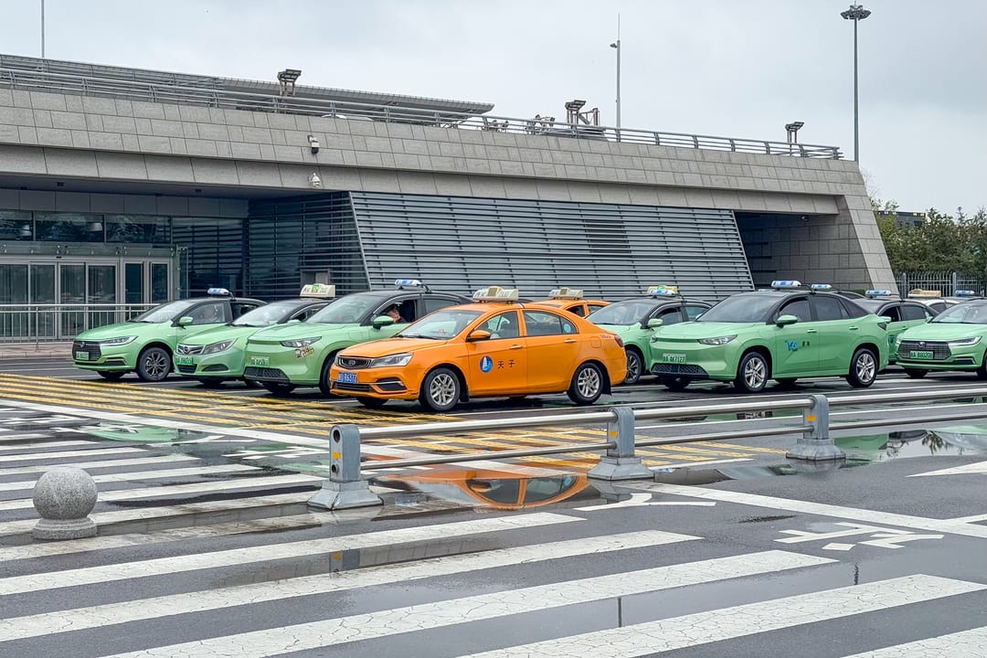 Taxis verdes y naranjas en fila en la parada oficial ante una terminal del aeropuerto de Xi’an Xianyang, en un día gris