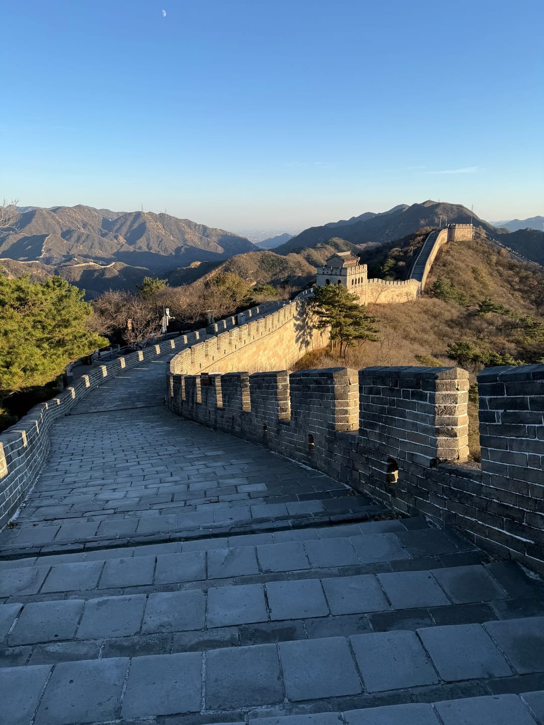 Un camminamento della Muraglia quasi vuoto a Badaling nel sole del tardo pomeriggio, che curva verso una torre di guardia