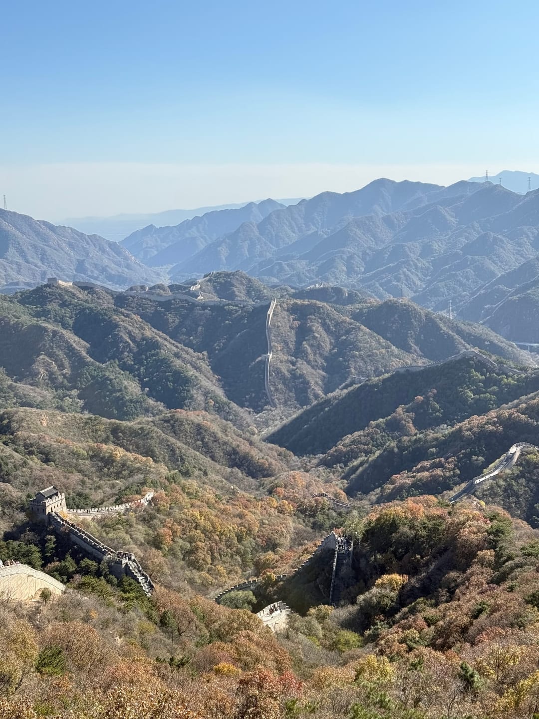 The Great Wall winding across forested ridges and down into a valley at Badaling, with layers of hazy mountains behind