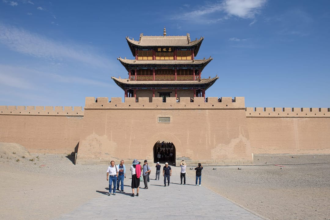 The three-storey gate tower of Jiayuguan Pass rising above an ochre fortress wall, with visitors walking in front
