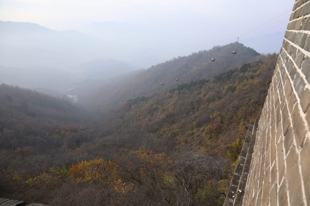Cable car cabins crossing a misty valley beside the Great Wall at Mutianyu, with autumn trees on the slopes