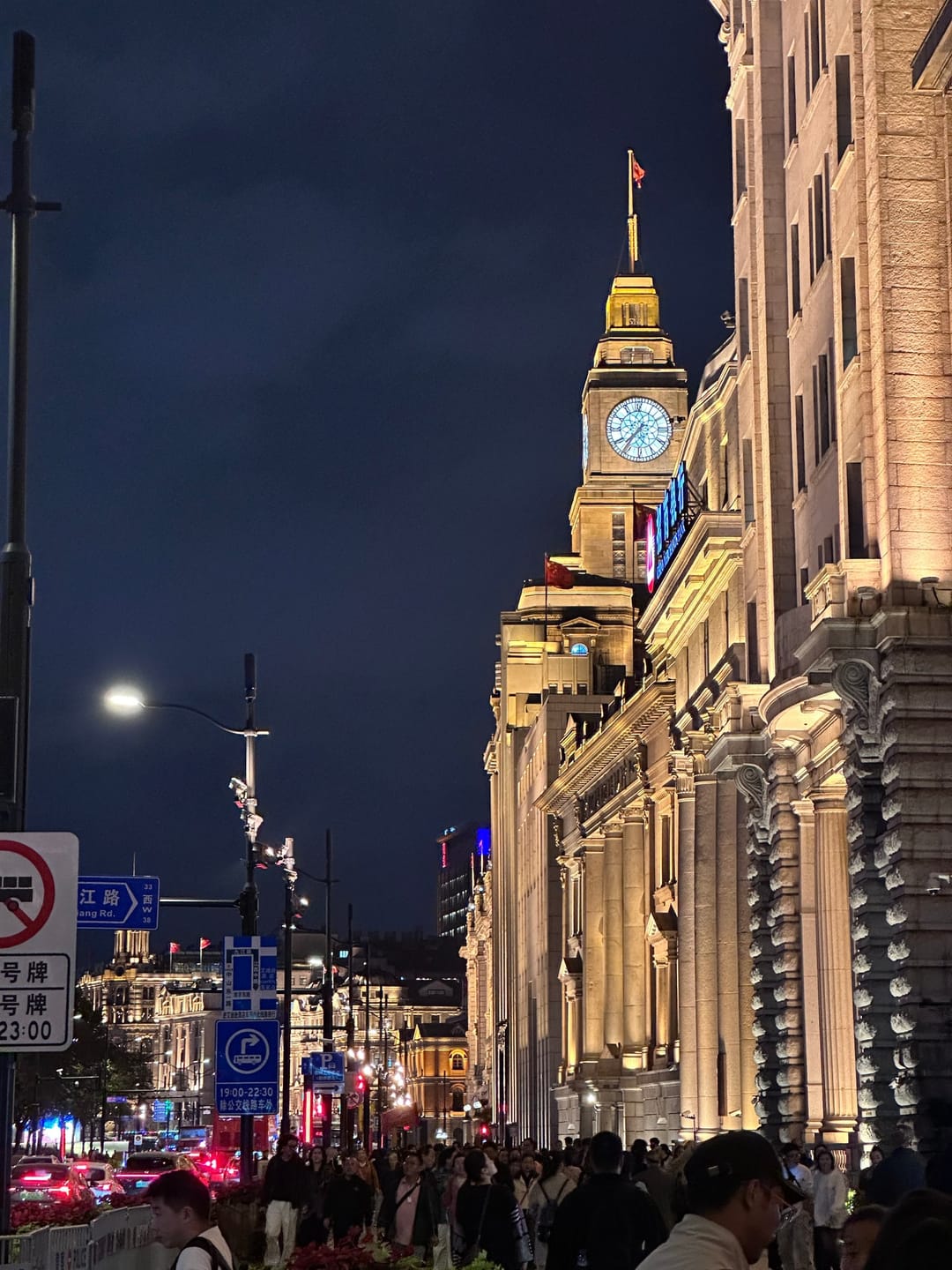 Der beleuchtete Uhrturm des Zollhauses am Bund bei Nacht, daneben weitere angestrahlte Fassaden und eine Straßenlaterne