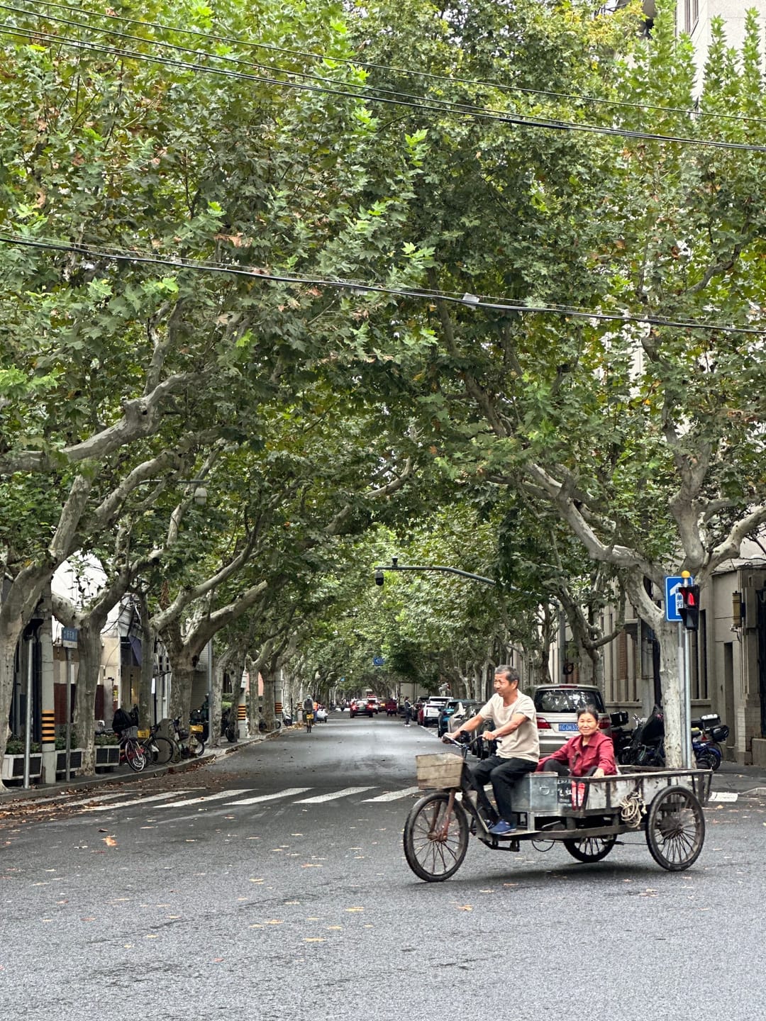 Un viale dell’ex Concessione francese sotto i platani, con una coppia in scooter, case basse e un semaforo