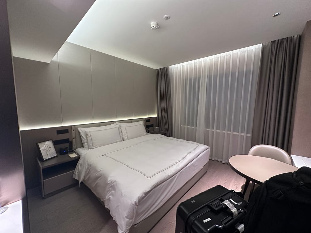 A modern double room with white bedding, grey curtains, a small round table and a suitcase on the floor