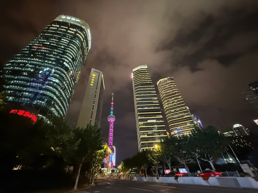 Office towers in Lujiazui seen from street level at night, with the pink lights of the Oriental Pearl Tower between them
