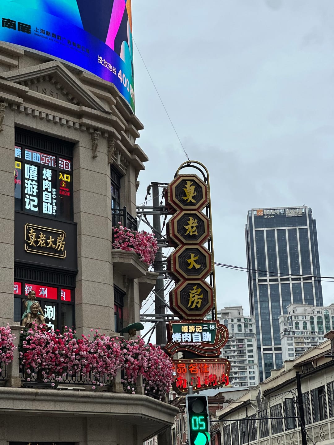 Insegne verticali di negozi su Nanjing Road East, tra cui una dorata a caratteri cinesi, davanti a un grattacielo di vetro