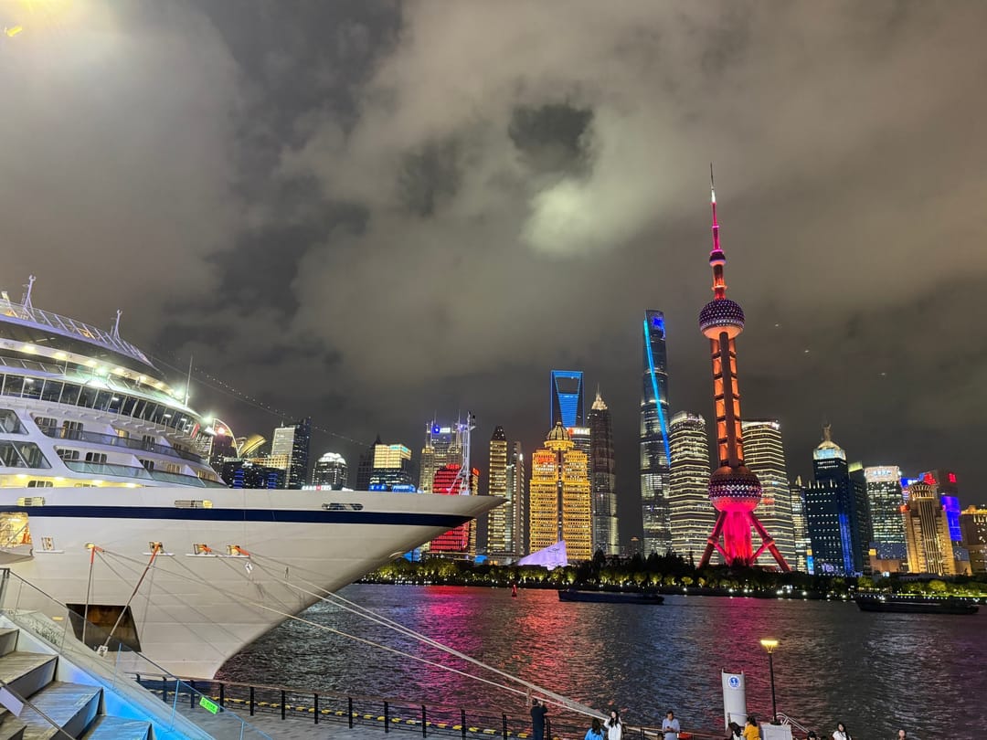 Una nave da crociera ormeggiata sul lungofiume del North Bund di sera, davanti allo skyline di Pudong e alla Oriental Pearl Tower rossa