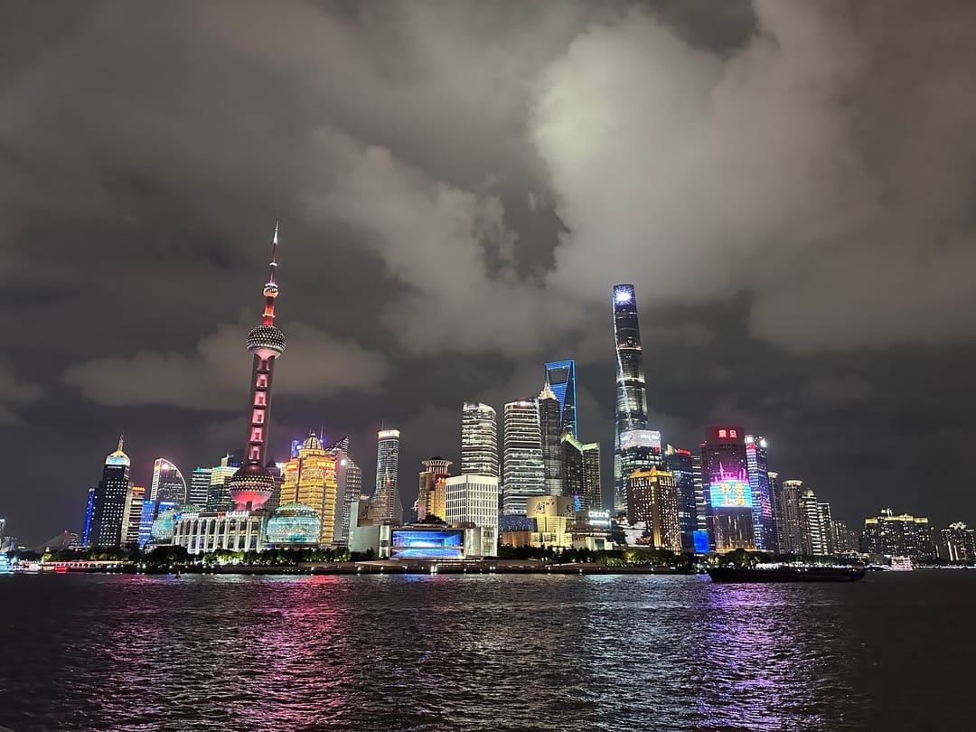 The Pudong skyline lit up at night across the Huangpu River, with the Oriental Pearl Tower on the left and the Shanghai Tower on the right