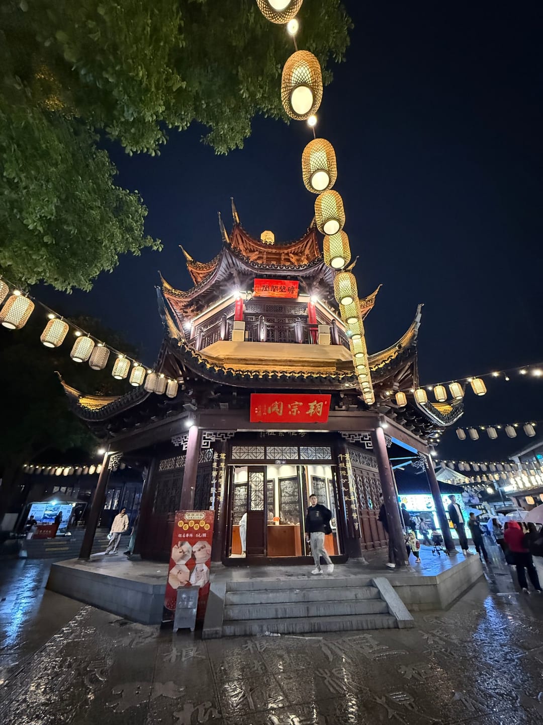 Un padiglione a più piani illuminato da lanterne la sera lungo via Shantang a Suzhou, con passanti davanti
