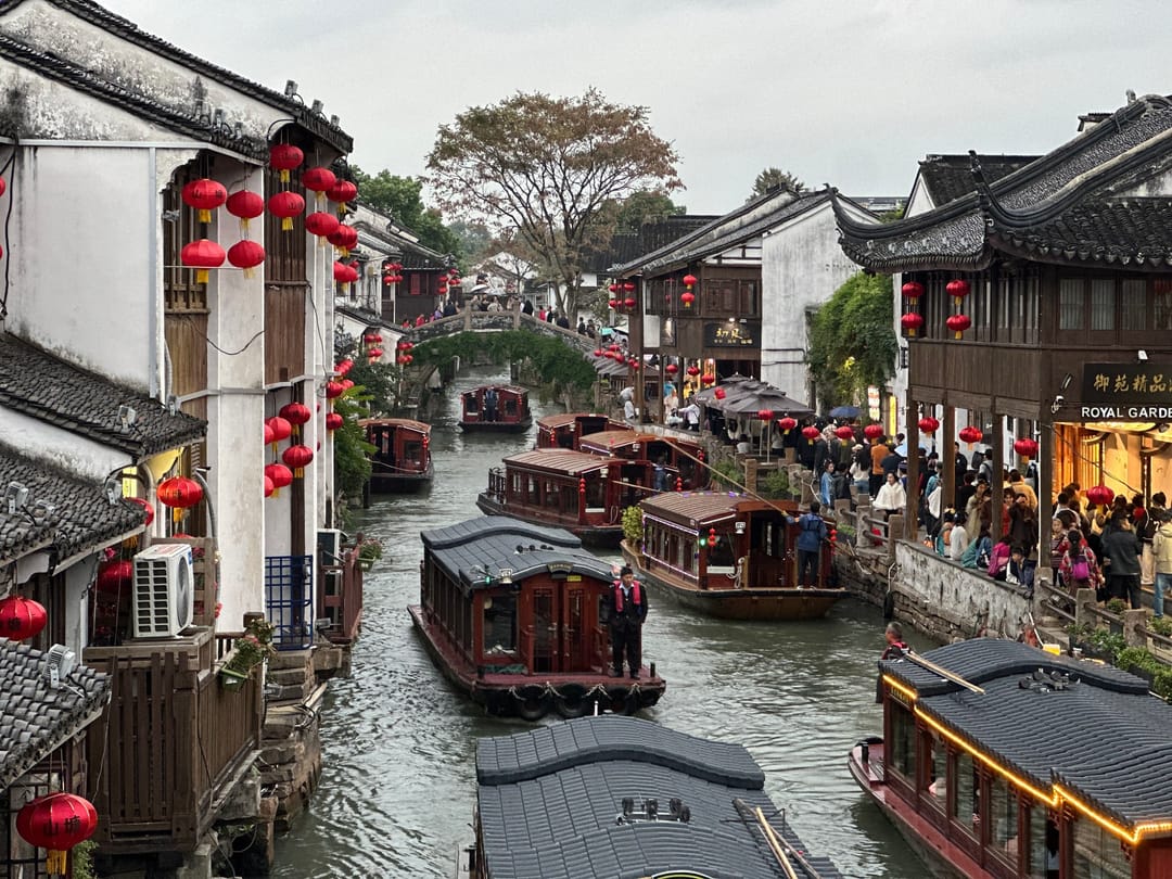 Tourist boats moored along a canal on Shantang Street in Suzhou, between white-walled houses hung with red lanterns