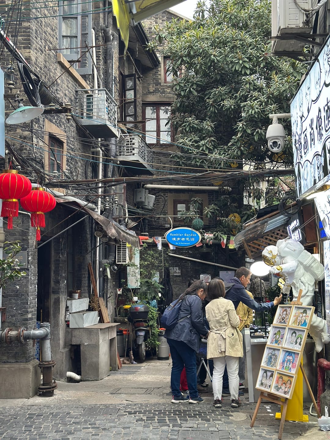 Un vicolo di Tianzifang con lanterne rosse, insegne di negozi e visitatori tra le case basse e i fili elettrici