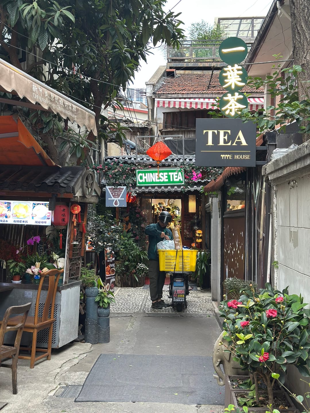 Eine schmale Gasse in Tianzifang mit einem Teeladen, roten Lampions und einem Lieferroller vor den Läden
