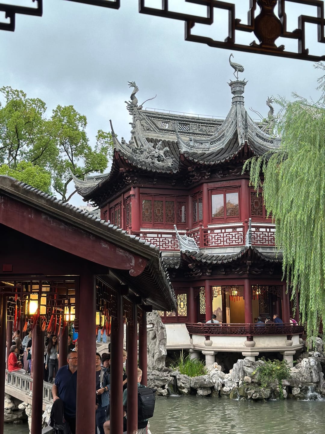 A two-storey pavilion with upturned eaves and red lattice windows in Yu Garden, framed by a weeping willow