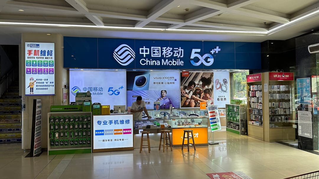 Mostrador de una tienda 5G de China Mobile en un centro comercial, con móviles expuestos y un vendedor tras el cristal