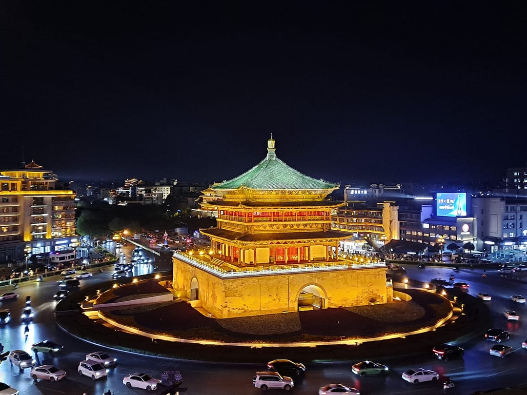 La Torre de la Campana de Xi’an iluminada en dorado de noche en el centro de su rotonda, con el tráfico girando alrededor