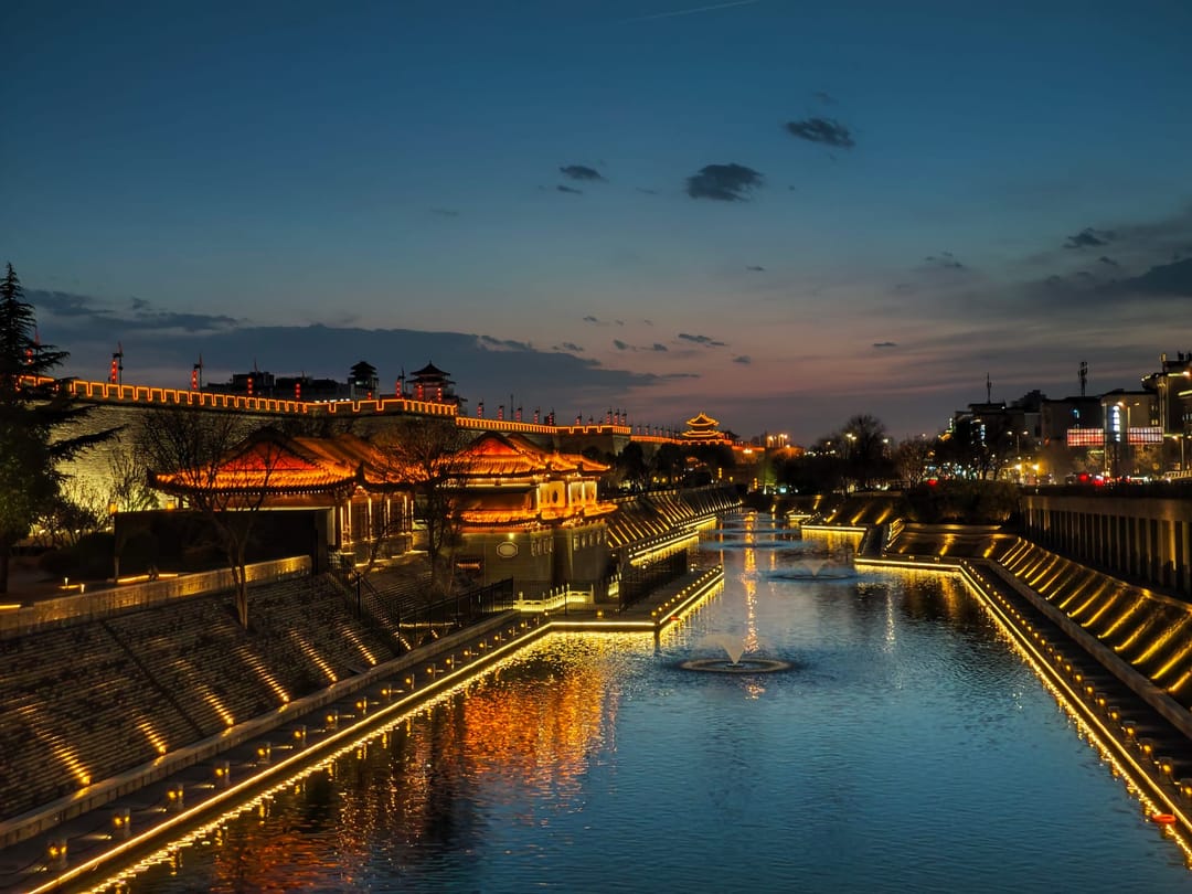 El foso y la esquina noreste de la muralla de Xi’an iluminada al anochecer, con fuentes en el agua